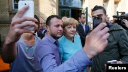 Берлиндегі босқындар орталығында канцлері Ангела Меркельмен (ортада) суретке түсіп тұрған мигранттар. Германия, қыркүйек 2015 жыл.