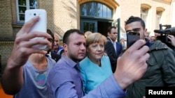 Syrian and Iraqi migrants take selfies with German Chancellor Angela Merkel in Berlin on September 10, 2015.