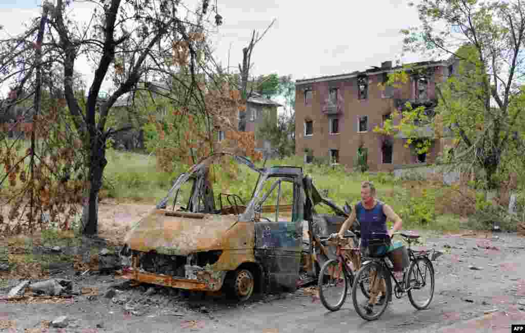 A resident pushes two bicycles past a burnt vehicle in the village of Semenivka, near Slovyansk, Ukraine, on July 13. (AFP/Genya Savilov)