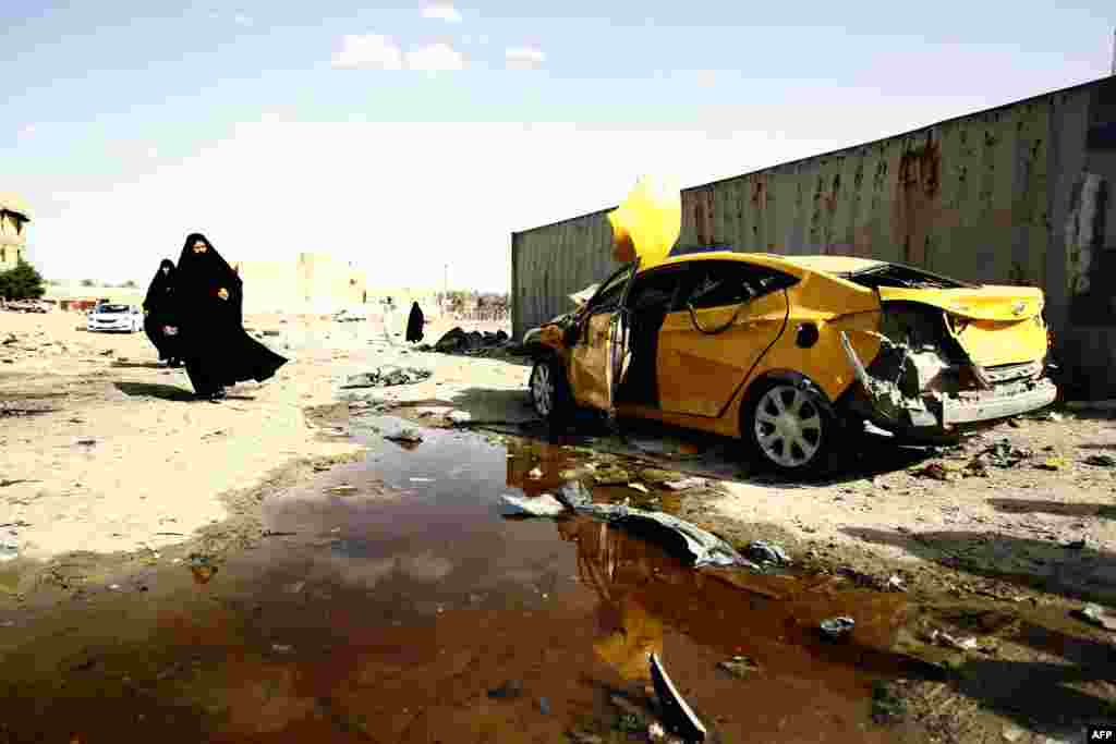 Iraqi women walk past a damaged car following a twin suicide bombing claimed by the Islamic State (IS) group in the southern Iraqi city of Samawah, deep in Iraq&#39;s Shi&#39;ite heartland. (AFP/Haidar Hamdani)