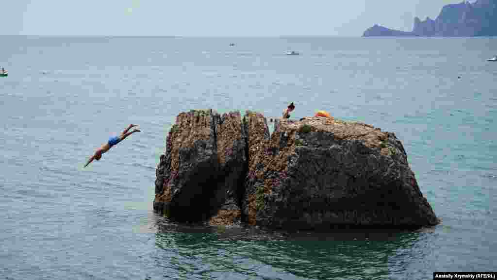 Дети прыгают с валуна в море на мысе Алчак, недалеко от Судака. Посмотреть на пейзажи Алчака можно в фотогалерее