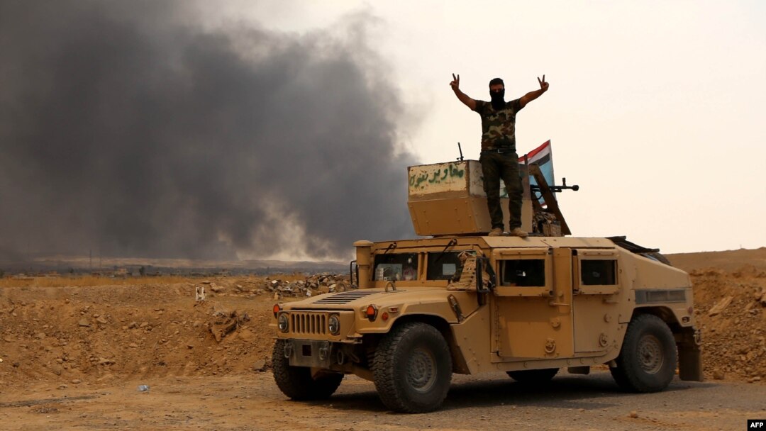 A member of Iraqi government forces flashes the sign for victory as he stands on a military vehicle while smoke billows from oil wells set ablaze by Islamic State militants before they fled the region of Qayyarah late last month. 