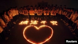 Студенты и учителя стоят вокруг свечей, зажженных в честь жертв взрывов в Тяньцзине. 