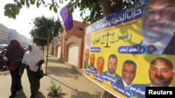 Egyptian women walk beside an election poster for the Muslim Brotherhood's "Freedom and Justice Party'" outside a polling station in Cairo.