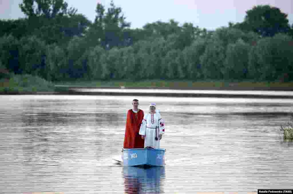 A couple in ethnic costumes stand in a boat on the Pripyat River in the town of Turau.
