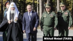 Patriarch Kirill (left) walks with Russian President Vladimir Putin (left to right), Defense Minister Sergei Shoigu, and Valery Gerasimov, chief of the General Staff of the Russian Armed Forces, near Moscow in September. Critics say the Russian Orthodox Church serves the interests of the state.