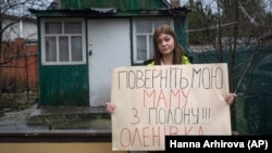 Alina Kapacina egy plakátot tart a kezében, amelyen ez áll: „Hozzátok vissza anyámat a fogságból. Olenivka”