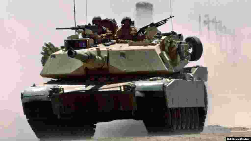 Un tanc M1A1 Abrams al pușcașilor marini americani rulează cu viteză pe o autostradă în apropiere de un punct de&nbsp; control militar de la Fallujah, 1 iulie 2004. Se crede că armata Statelor Unite are în dotare 2.509 de tancuri Abrams în diferite versiuni, și încă 3.700 în depozite.