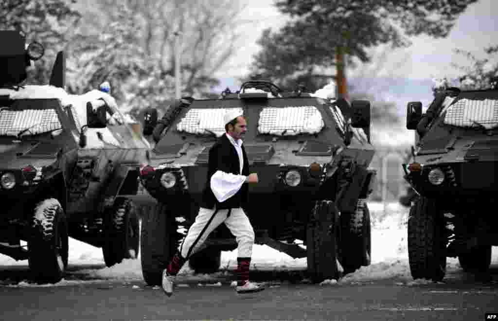 A member of a Kosovar folklore group runs past armored vehicles in Pristina during celebrations marking the fifth anniversary of the Kosovo Security Force (KSF).