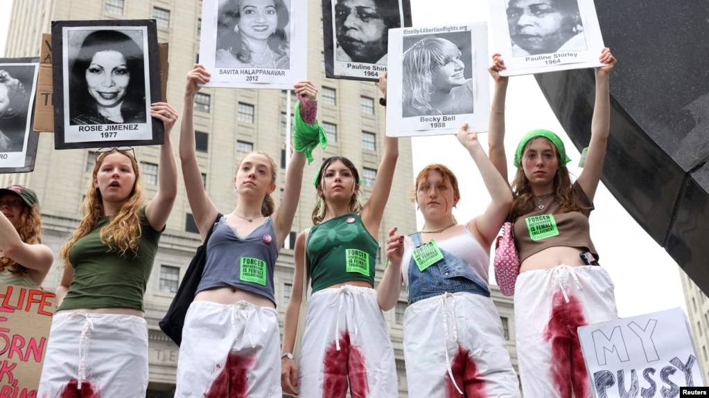 Жени в Ню Йорк протестират срещу забраната на абортите. Те носят снимки на жени, починали заради забраните за аборт в различни държави по света