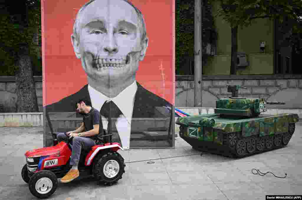 A member of the Roma ARESEL NGO pulls a mockup of a Russian tank past a satiric portrait of Russian President Vladimir Putin during a protest against Russia&#39;s invasion of Ukraine in front of the Russian Embassy in Bucharest.