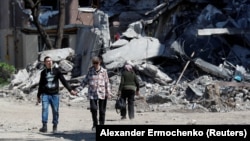Местные жители проходят мимо разрушенного здания в Мариуполе, 12 мая 2022 года