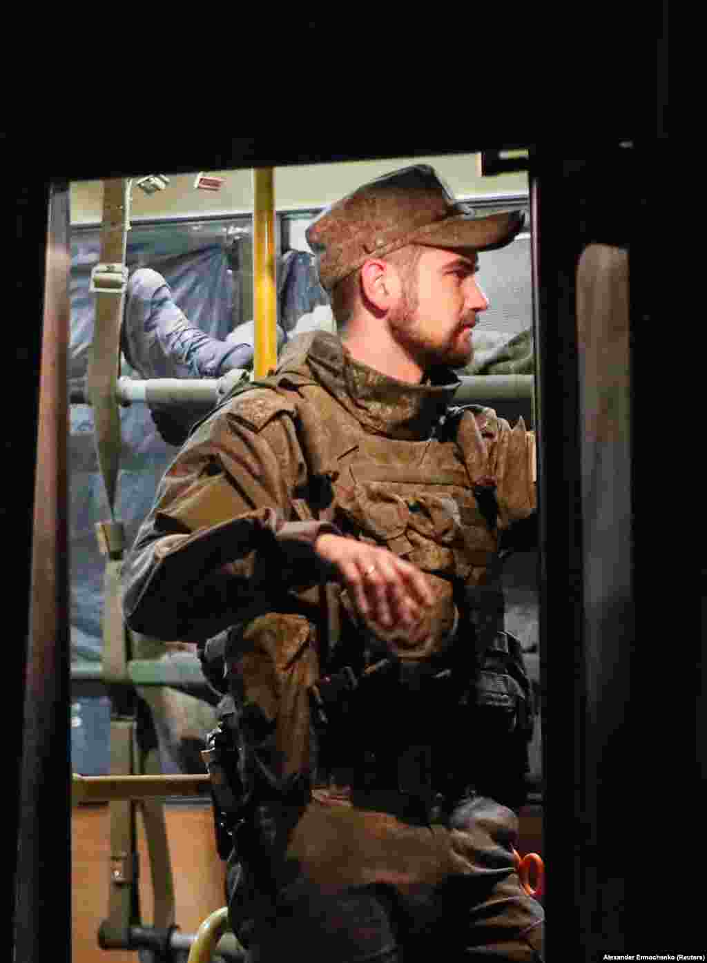 Сепаратистички борец стои на стража пред автобус што превезува ранети украински војници од Мариупол.