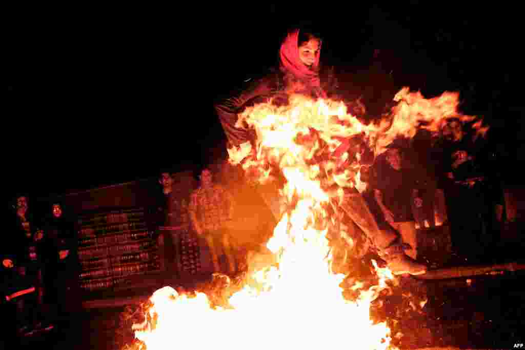 A woman jumps over a bonfire in southern Tehran during the Fire Feast held before Norouz celebrations. (AFP/Behrouz Mehri)