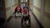 Natașa Stepanenko (stânga) și fiul ei, Yarik (11 ani) în timp ce împinge scaunul cu rotile al surorii sale gemene, Yana, pe holul unui spital din Liov, 12 mai 2022. Ei au fost răniți pe 8 aprilie, când o rachetă rusească a lovit gara din orașul Kramatorsk, în estul țării.