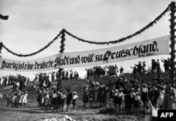  Снимка от 1939 година на хора, отправили фашистки привет под надпис на немски език. Той е с откъс на Хитлер и гласи: 