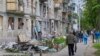 Localnici din Harkov, al doilea oraș ca mărime din Ucraina, trec pe lângă o clădire rezidențială avariată de un bombardament rusesc. Fotografie din 25 mai 2022. 
