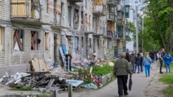 Localnici din Harkov, al doilea oraș ca mărime din Ucraina, trec pe lângă o clădire rezidențială avariată de un bombardament rusesc. Fotografie din 25 mai 2022. 