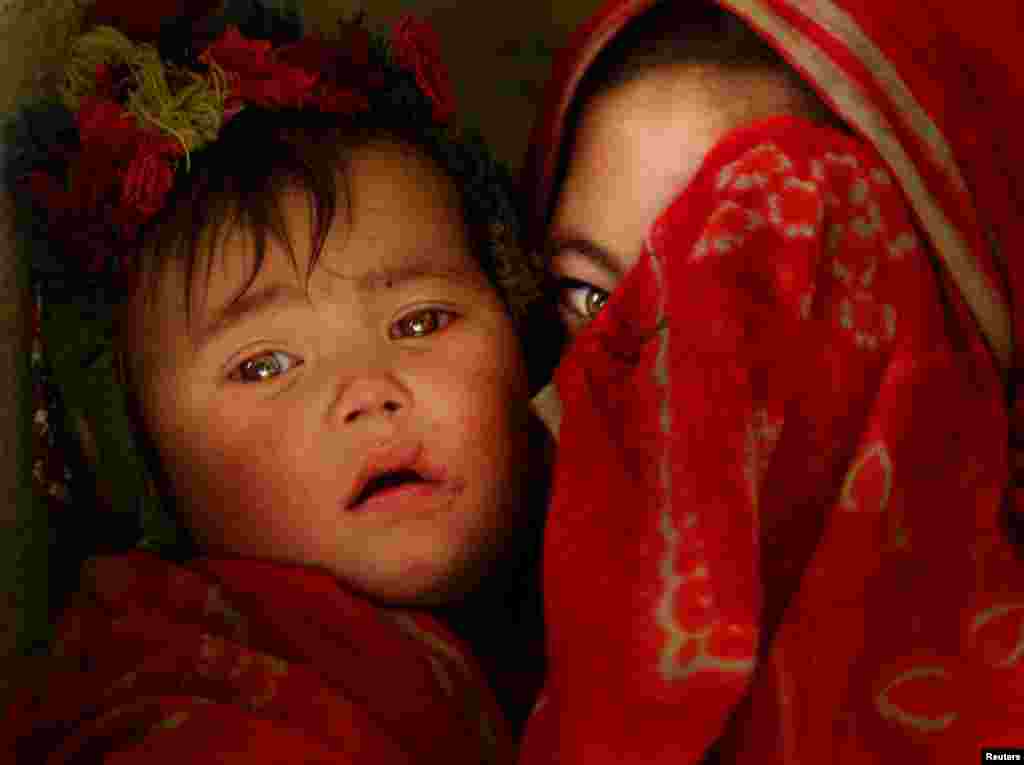 A Hazara girl covers her face as she holds a child in a cave in Bamiyan, Afghanistan, in December 2011.