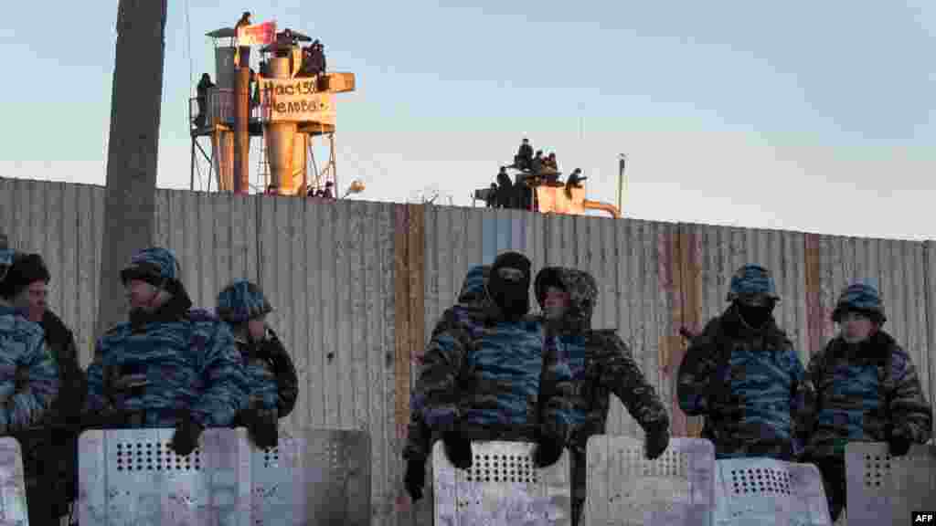 Police officers in riot gear cordon off the prison, with protesting inmates in the background.