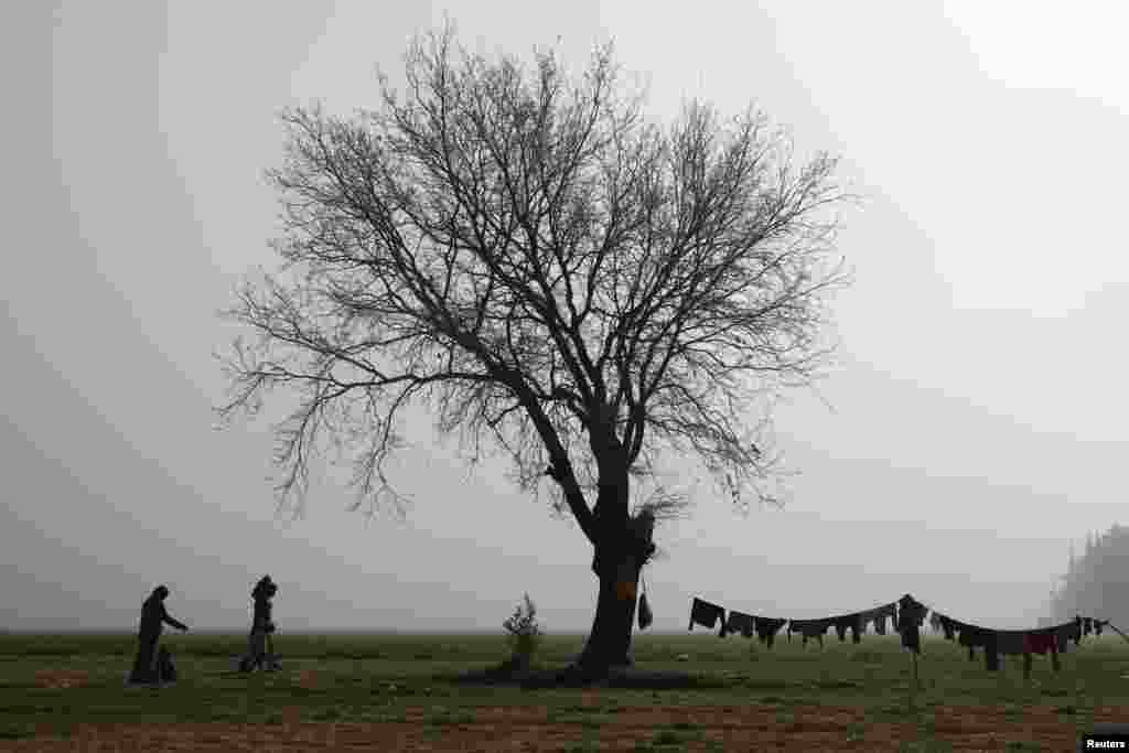 Сям&#39;я ідзе праз поле каля часовага лягеру мігрантаў і ўцекачоў на грэцка-македонскай мяжы. (Фота Reuters)&nbsp;