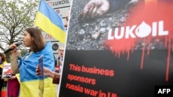 A woman wrapped in a Ukrainian flag addresses protesters gathered near the Lukoil headquarters in Brussels on May 13. Lukoil been under U.S. sanctions since 2014.