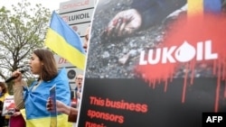 A woman wrapped in a Ukrainian flag addresses protesters in Brussels calling for a boycott of the Russian oil company Lukoil.