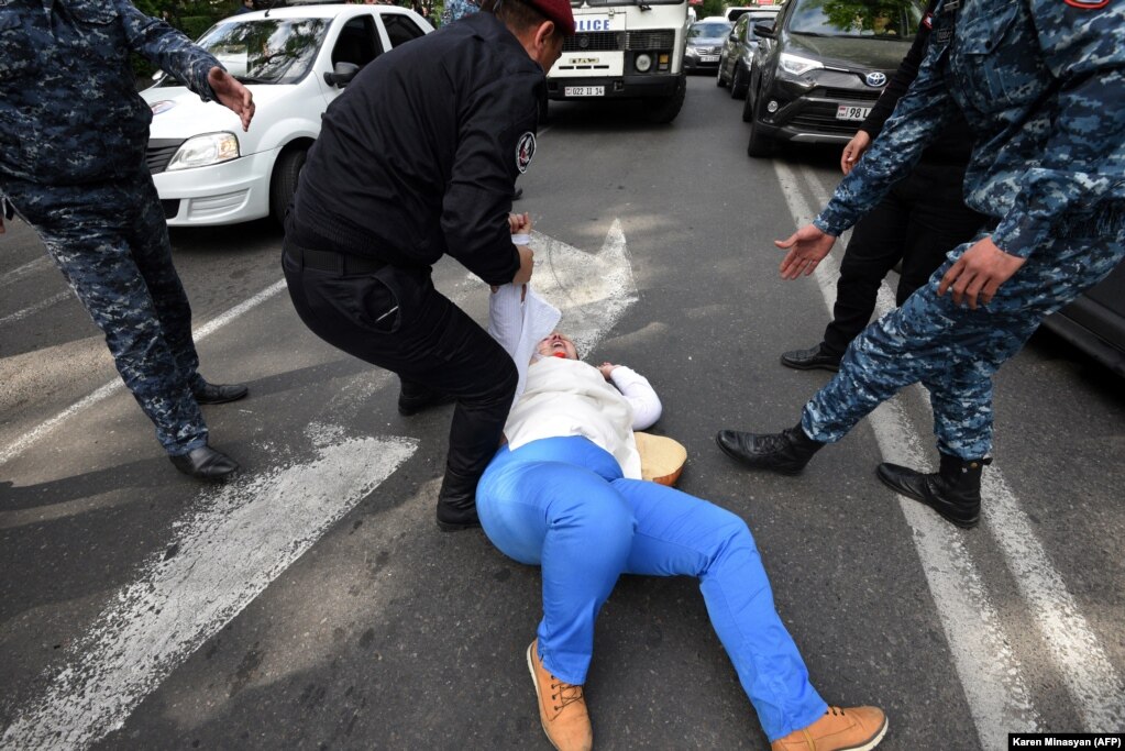 Një grua protestuese shihet e shtrirë në rrugë në qendër të Jerevanit, ndërsa policia përpiqet ta ndalojë. Një të moshuare i është thyer krahu gjatë trazirave të 18 majit.
