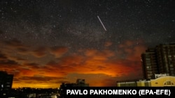  Фотография, сделанная с длинной выдержкой, показывает оранжевое свечение продолжающегося боя, проецируемое на облака, когда спутник (C, вверху) пересекает звездное небо над окраиной Харькова, Украина, 19 мая 2022 г. 