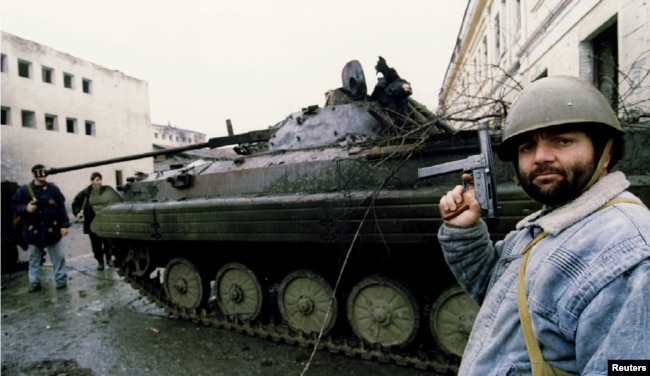 Militantët çeçenë duke qëndruar pranë një automjeti të blinduar rus, i shkatërruar në betejën për Groznin në janar të vitit 1995.