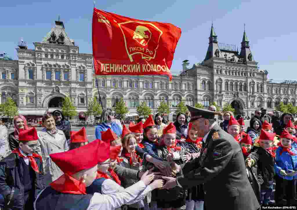 A gyerekek egy háborús veteránnal fognak kezet egy Lenin-zászló alatt. A Szovjetúnió idején a korabeli ifjúsági szervezetek célja az volt, hogy &bdquo;a gyerekek a lehető legkevesebb időt töltsék szabadon, állami kontroll nélkül&rdquo;