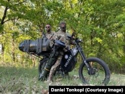 Luptători ucraineni pe o bicicletă electrică Delfast cu o armă antitanc.