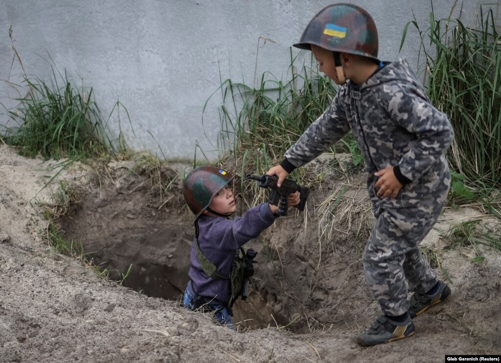 Fëmijët ukrainas ia kalojnë njëri-tjetrit armët lodra teksa luajnë pranë shtëpive të tyre në mes të pushtimit rus në fshatin Stojanka në rajonin e Kievit.