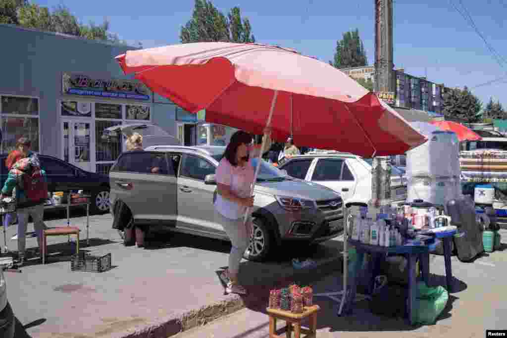 Egy nő napernyőt állít rögtönzött standja fölé Szlovjanszkban július 2-án. A helyiek az ingóságaikat próbálják&nbsp;a piacon eladni, hogy némi bevételhez jussanak vagy legalább elcserélhessék élelmiszerre