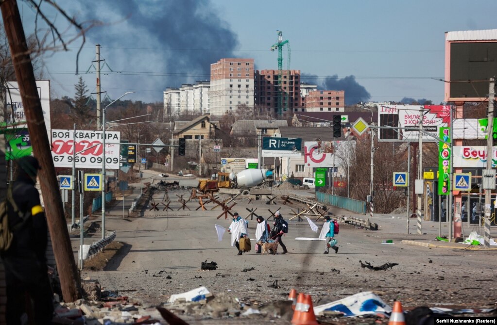 Civilians draped in sheets and carrying white flags cross a road that runs between Bucha and Irpin on March 11.