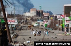 Civilians draped in sheets and carrying white flags cross a road that runs between Bucha and Irpin on March 11.