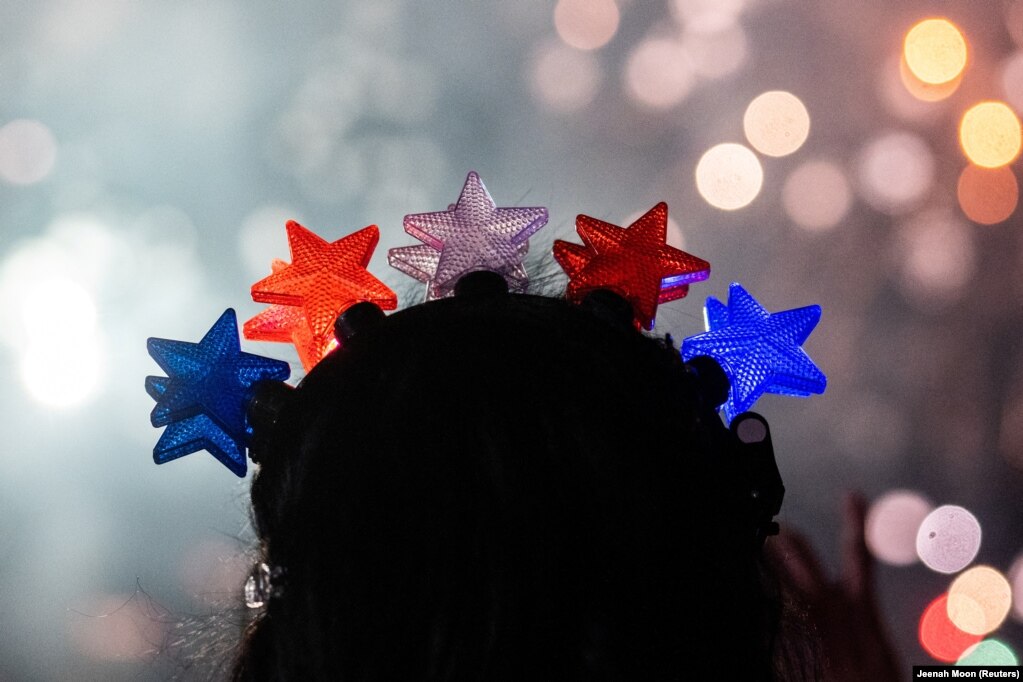 Një pjesëmarrëse me yje me ngjyrat e flamurit amerikan në kokë, duke shikuar një shfaqje fishekzjarrës, në Nju-Jork.
