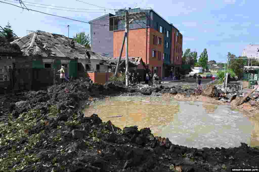 Bystanders and officials gather near a water-filled crater after the explosion of a Russian rocket in the northwestern outskirts of Kharkiv on June 26.