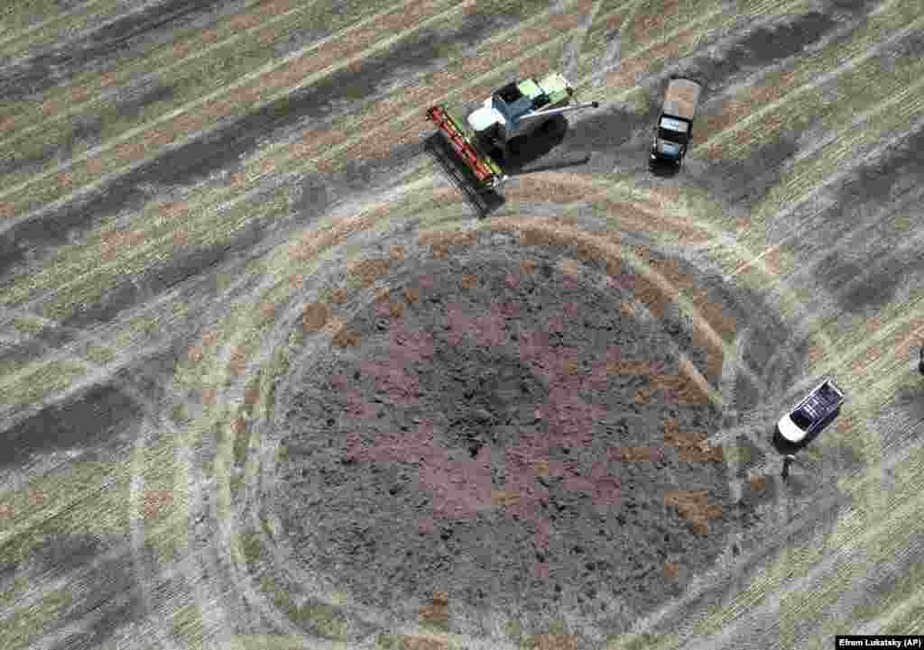 A crater left by a Russian rocket attack is seen as a farmer collects harvest in a field, 10 kilometers from the front line where a fierce battle was ongoing in Ukraine&#39;s Dnipropetrovsk region on July 4.