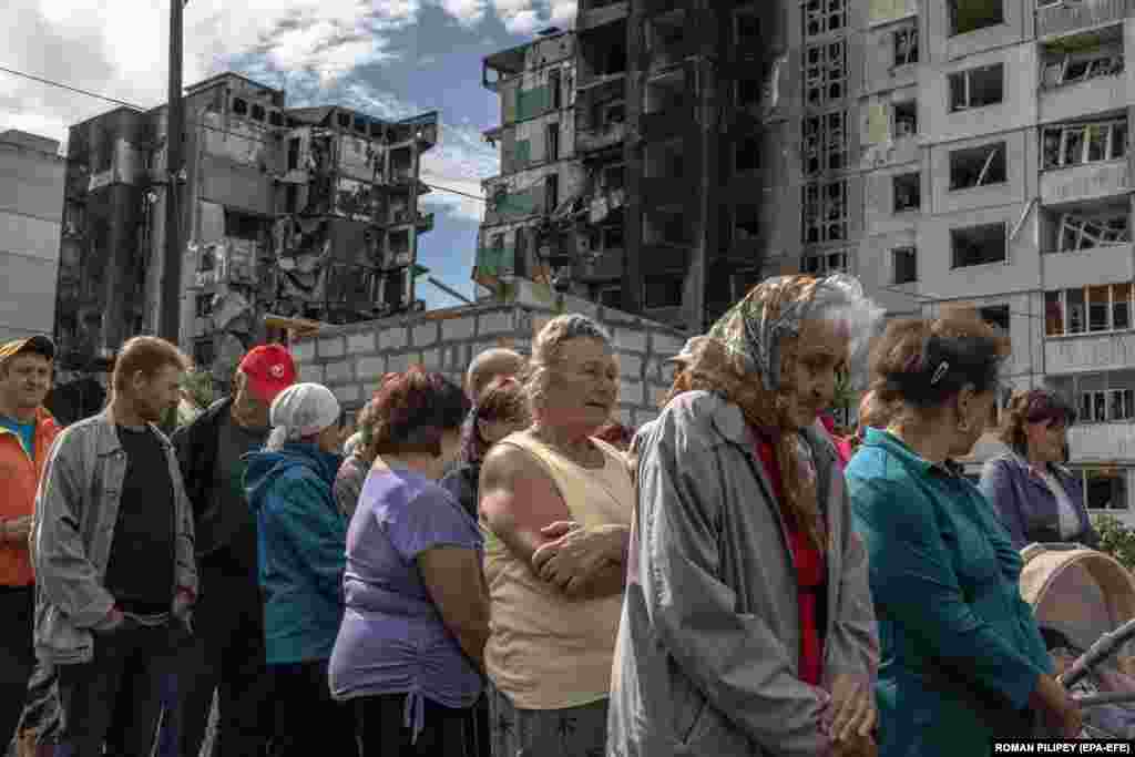 Banorët vendas duke pritur në radhë për ndihma humanitare, ndërsa prapa tyre shihet&nbsp; një ndërtesë banimi e dëmtuar nga sulmet ruse në Borodjanka, Ukrainë.