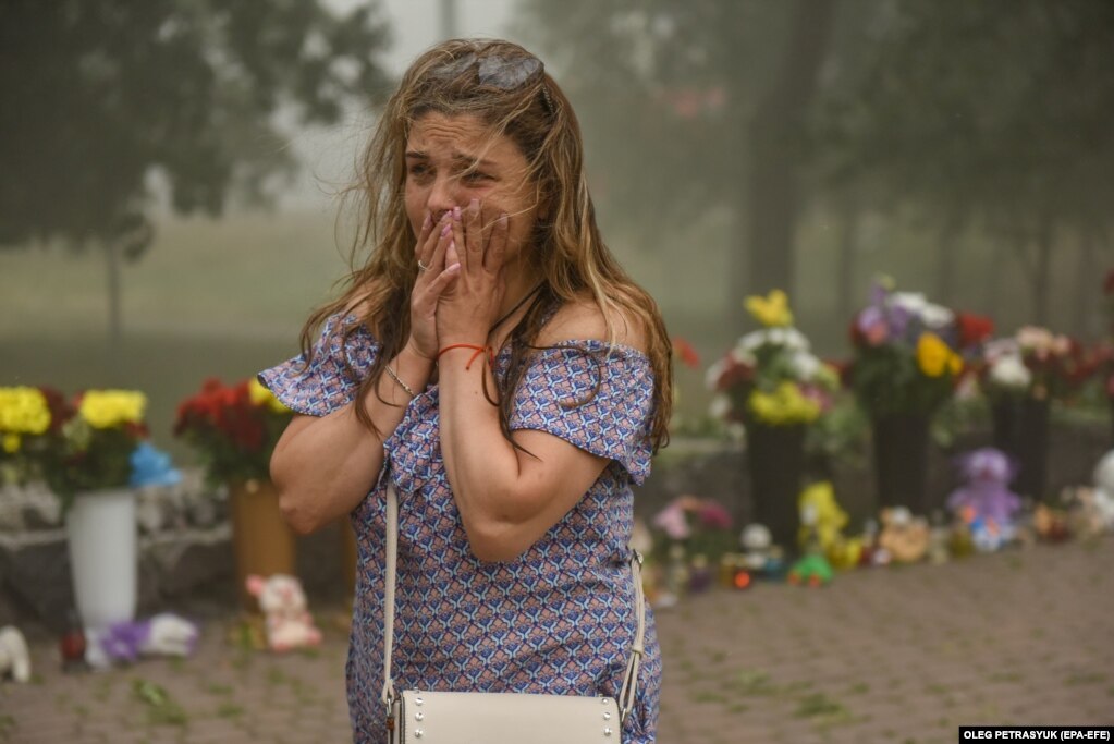 Një grua duke qarë&nbsp;ndërsa pas saj shihen lulet që njerëzit kanë&nbsp;sjellë&nbsp;në qendrën tregtare tashmë të shkatërruar Amstor në Kremençuk, Ukrainë, më 28 qershor, pasi një sulm me raketa ruse vrau të paktën 18 njerëz një ditë më parë.