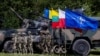 Польские (справа) и румынские (слева) солдаты стоят рядом с военной техникой и флагом НАТО у мобильного командного центра многонациональной дивизии НАТО «Северо-восток» возле деревни Шиплишки на северо-востоке Польши, 7 июля 2022 года