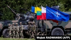 Польские (справа) и румынские (слева) солдаты стоят рядом с военной техникой и флагом НАТО у мобильного командного центра многонациональной дивизии НАТО «Северо-восток» возле деревни Шиплишки на северо-востоке Польши, 7 июля 2022 года