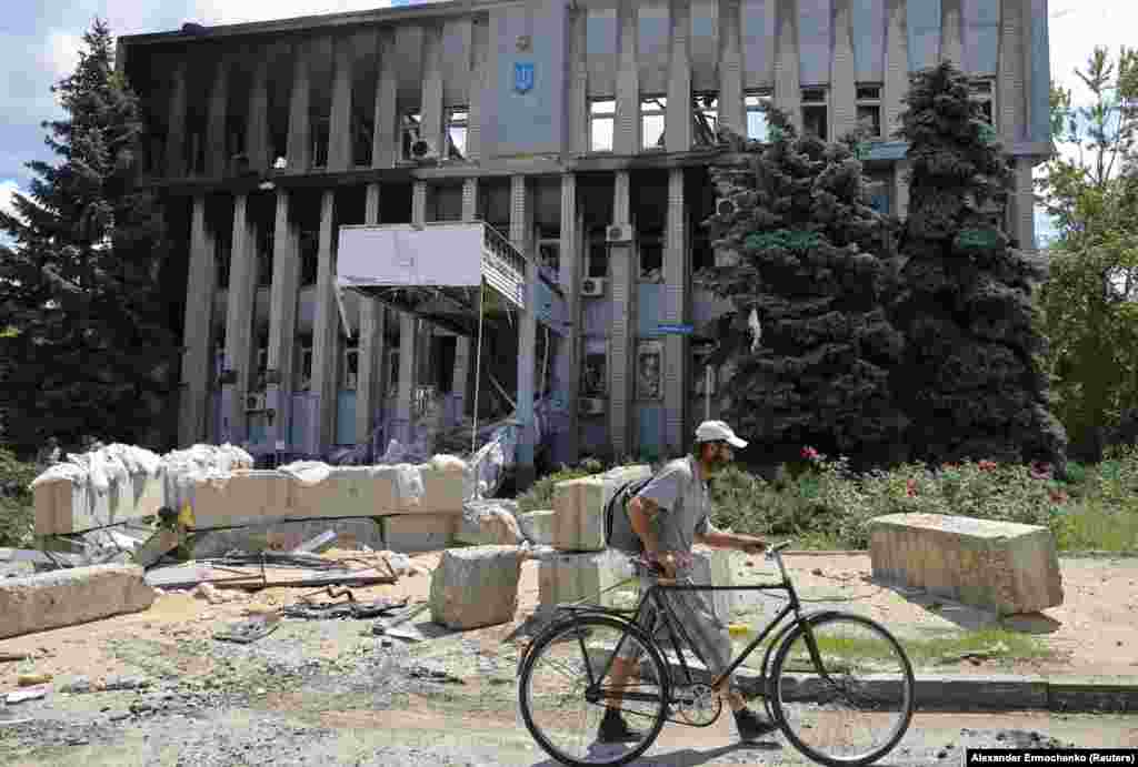 A local resident walks with a bicycle past a destroyed police department building.