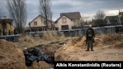 Український військовий біля братської могили з тілами мирних жителів, які, за словами очевидців, були вбиті російськими окупантами у Бучі, 6 квітня 2022 року