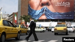A woman in Tehran walks past an anti-American billboard depicting US President Donald Trump and the Strait of Hormuz. 