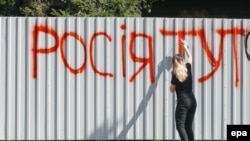 An activist sprays the words "Russia is here" on the barrier around Inter TV in Kyiv on September 5.