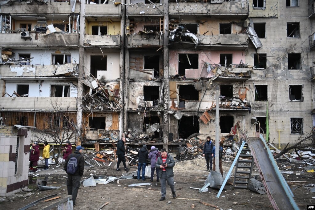 Njerëzit qëndrojnë jashtë një ndërtese banimi të shkatërruar në natën e dytë të sulmeve ruse, Kiev, 25 shkurt 2022. 