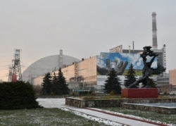 Monument în fața uriașului dom de protecție construit deasupra sarcofagului celui de-al patrulea reactor distrus al centralei nucleare de la Cernobîl. Fotografie realizată la 8 decembrie 2020.