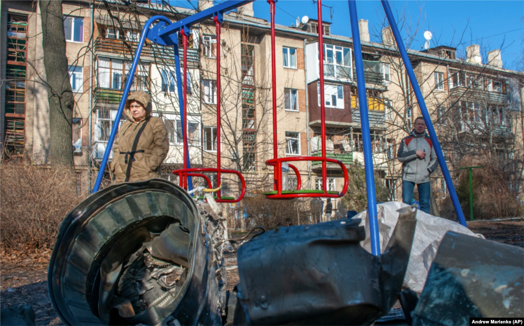 Чоловік і жінка стоять біля уламків військової техніки на вулиці після очевидного удару російської авіації по Харкові